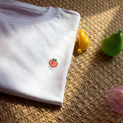 White t-shirt with peach design by Out Now! folded neatly in a stylish setting, perfect for LGBTQ+ pride and icebreakers.